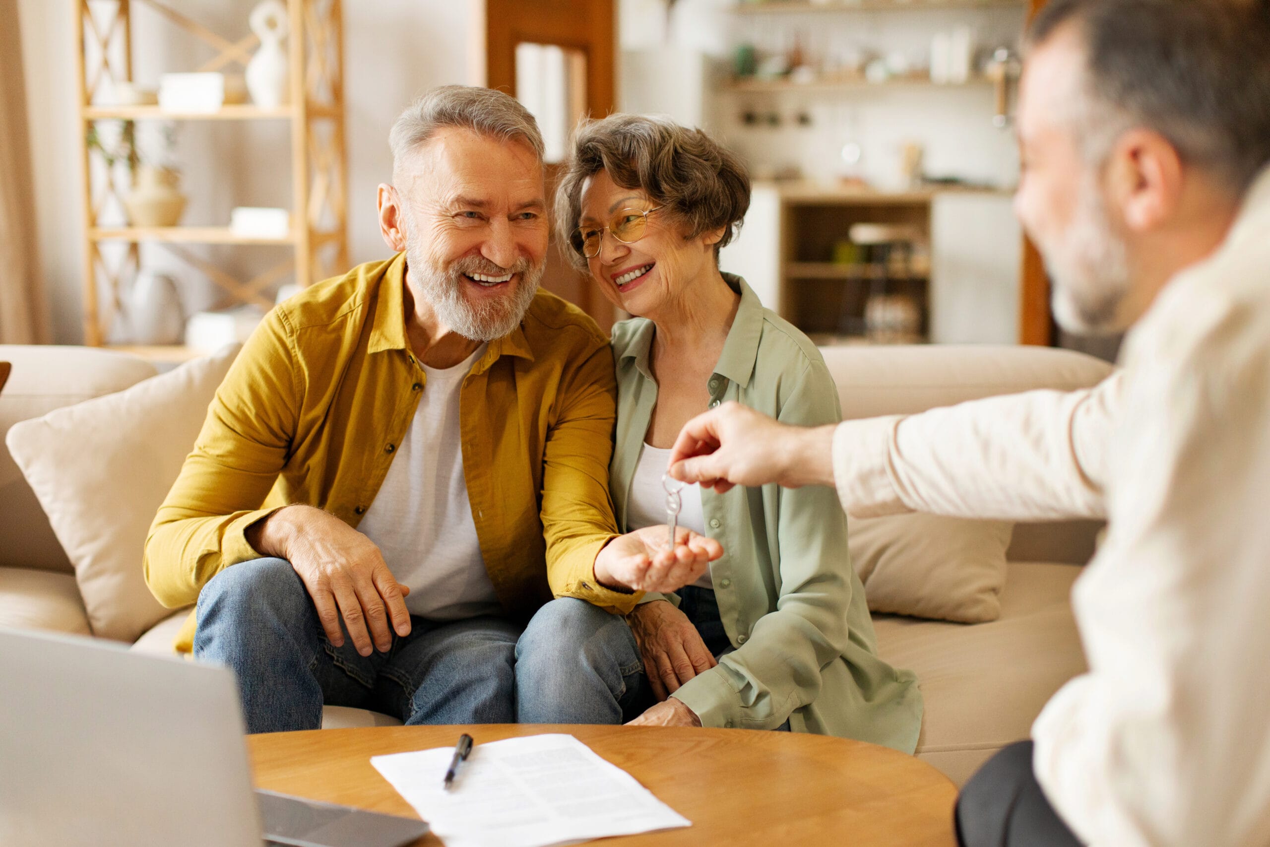 Agent giving keys from new home to excited senior spouses, buying own property, sitting on couch indoors. House Purchase and rent concept